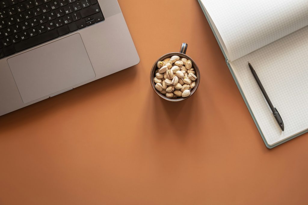 Flat lay, laptop, notepad and pistachio nuts.